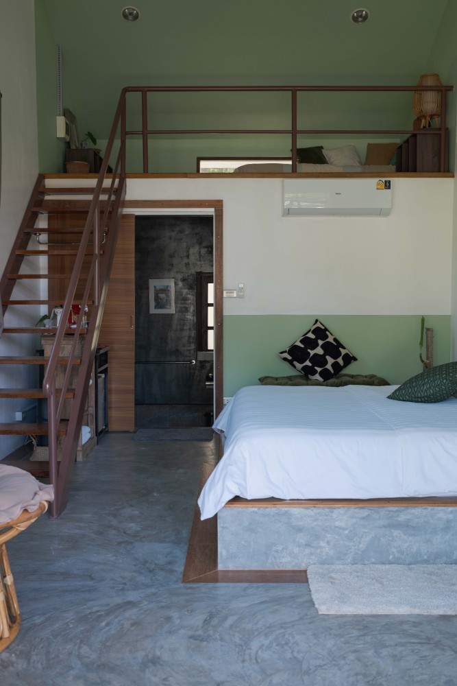 View from the mezzanine down to a double bed and green artwork in a garden room at Tree Roots Retreat, Mae Ramphueng, Rayong.