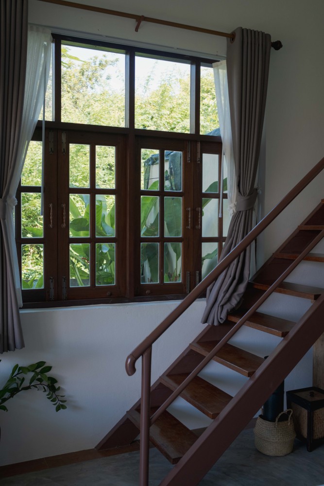 Mezzanine in a garden room at Tree Roots Retreat, Mae Ramphueng, Rayong, with the double bed and green artwork below and a desk beside the stairs.