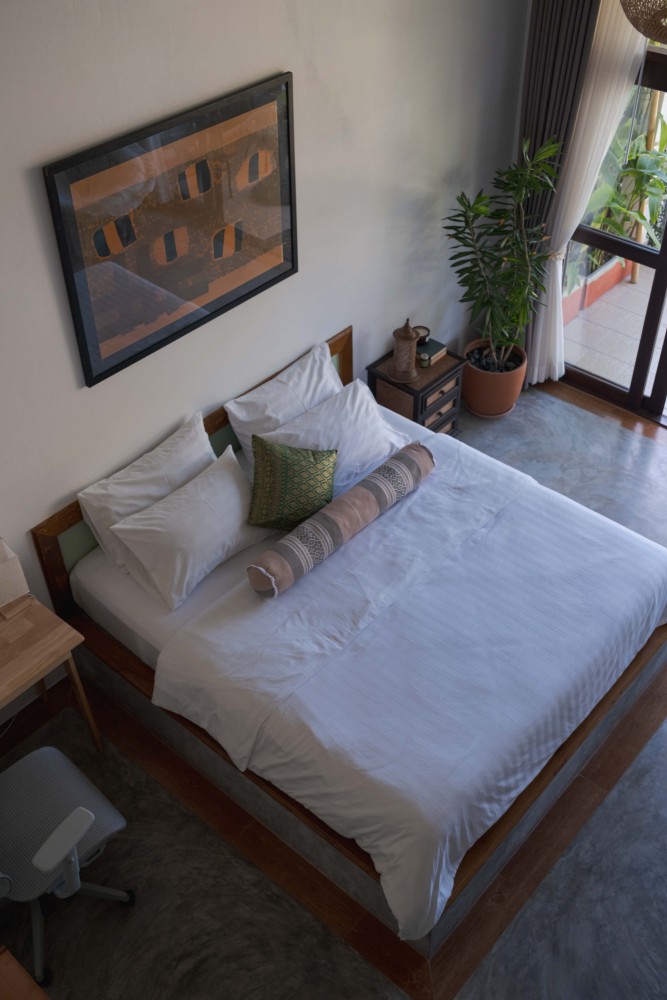 Double bed with white linen and a green abstract painting above the headboard in a garden room at Tree Roots Retreat, Mae Ramphueng, Rayong.