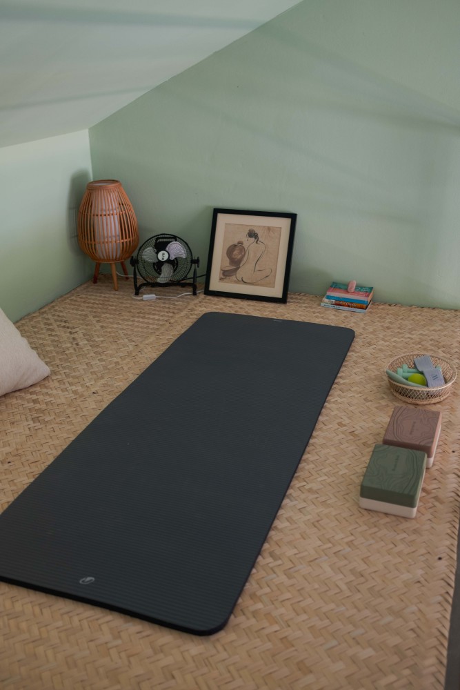 A yoga mat on the floor of a garden room at Tree Roots Retreat, Mae Ramphueng, Rayong, beside the double bed and a green painting.