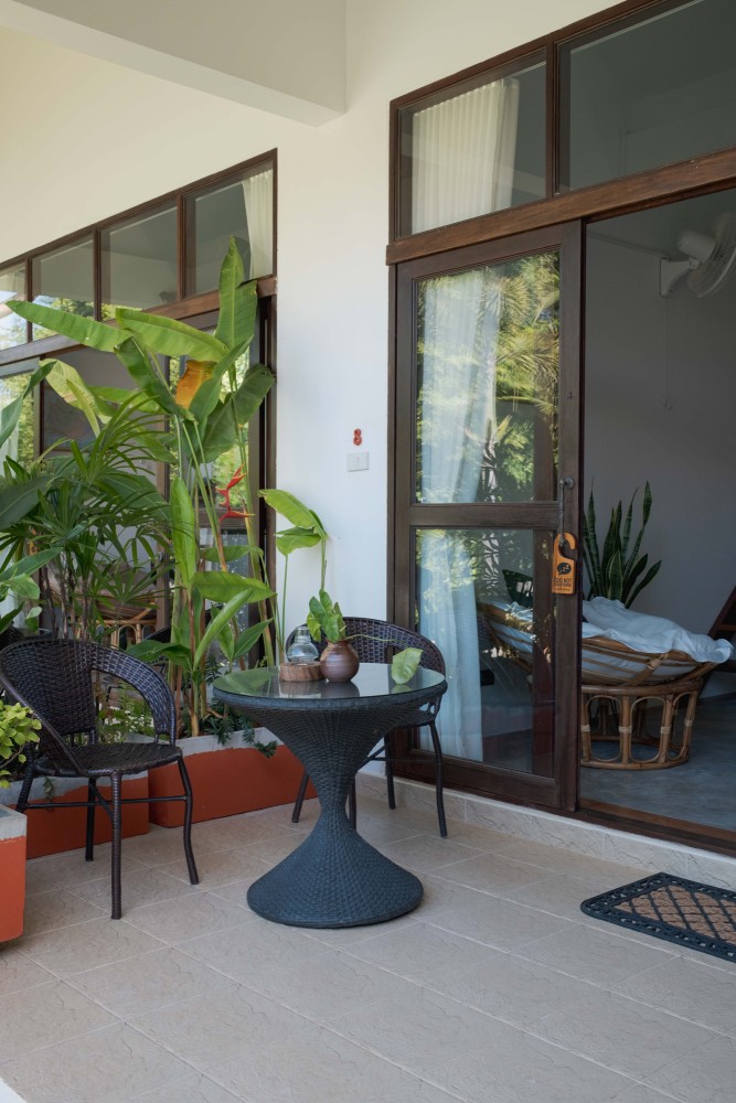 Veranda at Tree Roots Retreat, Mae Ramphueng, Rayong, with a lounge chair, a wicker chair, a monstera, and the pool beyond.