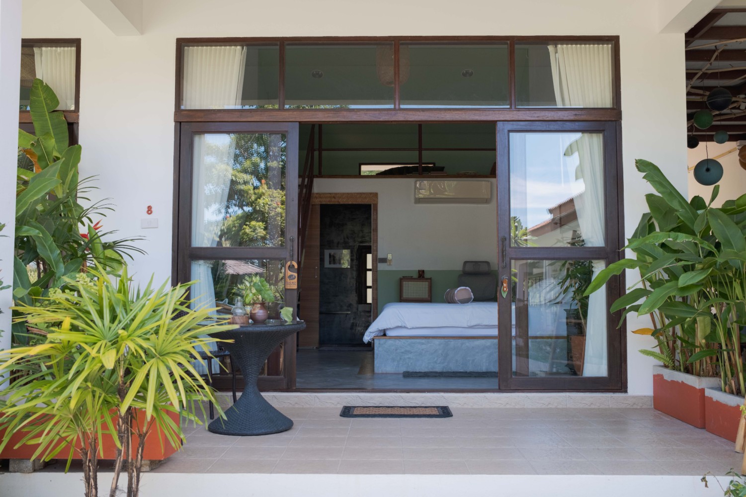 เก้าอี้หวายสองตัวบนระเบียงที่ Tree Roots Retreat แม่รำพึง ระยอง มองออกไปเห็นสระน้ำและสวนเขตร้อน