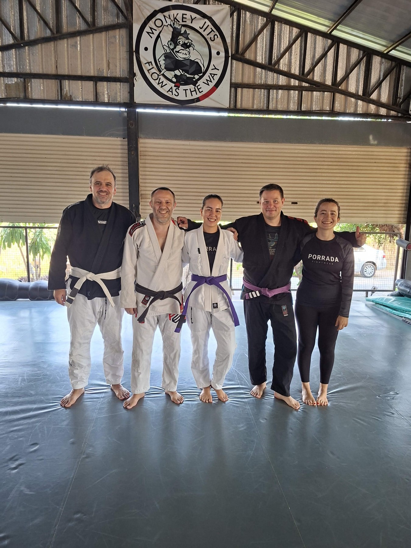 Claire in her purple belt gi with the Tree Roots Retreat Brazilian Jiu-Jitsu team in Rayong, Thailand &mdash; five practitioners from blue to black belt after a training session at the Mae Ram Phueng jiujitsu retreat.