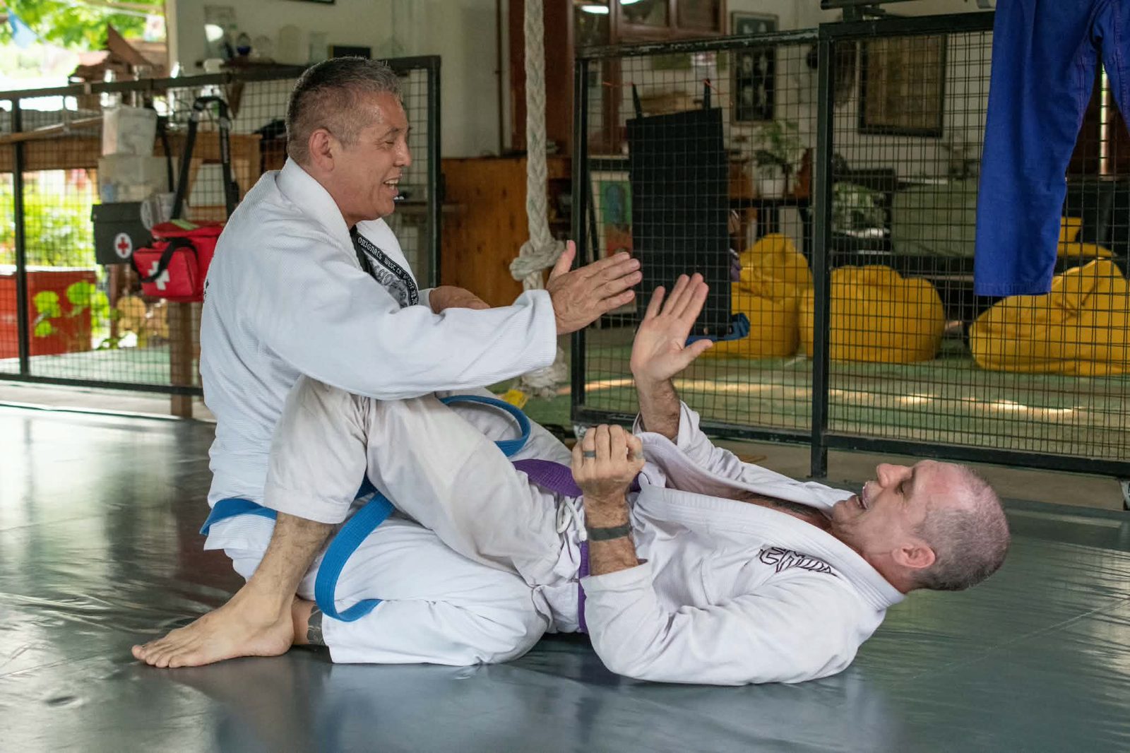 Brazilian Jiu-Jitsu training at Tree Roots Retreat in Rayong, Thailand &mdash; Michael rolling on the mat with a training partner, smiling mid-technique, at the Mae Ram Phueng jiujitsu retreat.