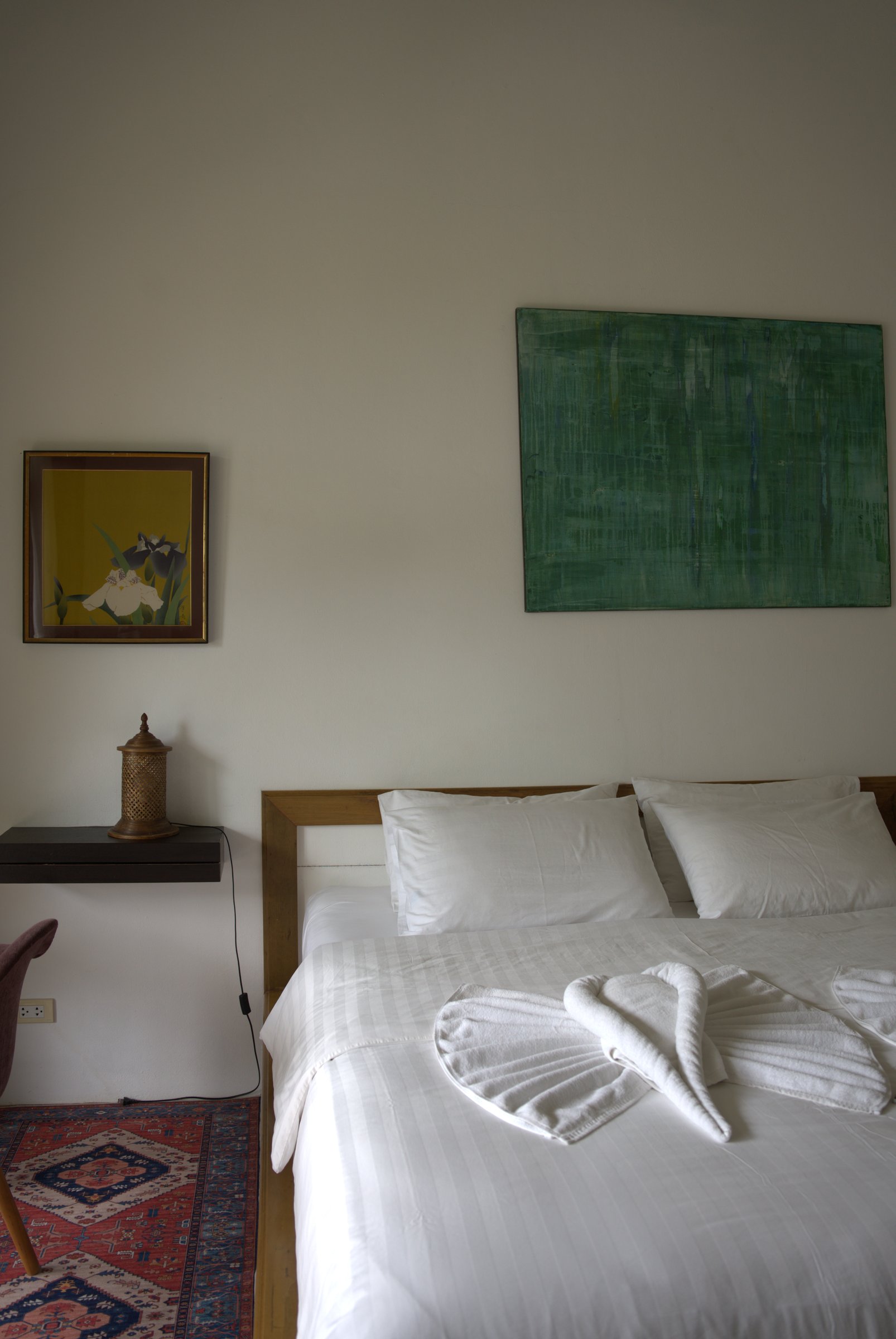 Garden room at Tree Roots Retreat, Rayong, with a king bed in white linen, a wooden headboard, and a green painting on the wall.