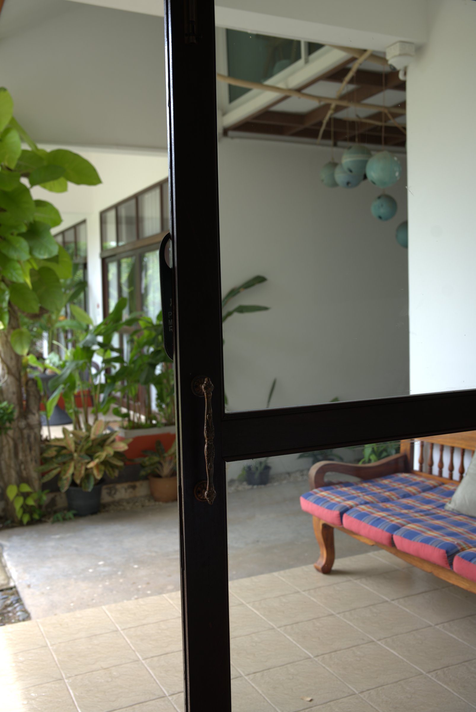 Sliding glass door of a garden room at Tree Roots Retreat, Rayong, opening onto a terrace daybed and tropical plants.
